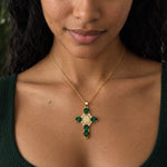 Pendentif croix doré avec pierres précieuses vertes, porté par Aline