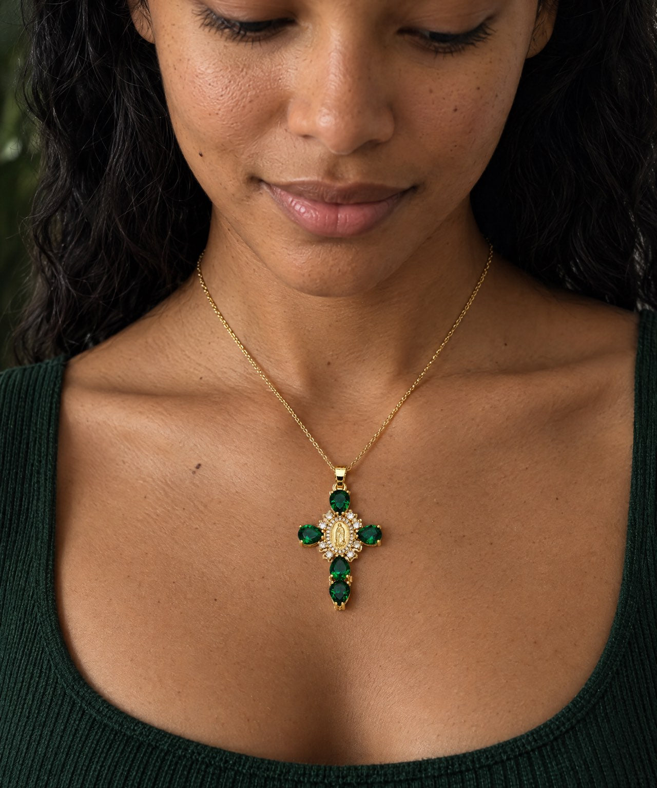 Pendentif croix doré avec pierres précieuses vertes, porté par Aline