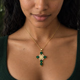 Pendentif croix doré avec pierres précieuses vertes, porté par Aline