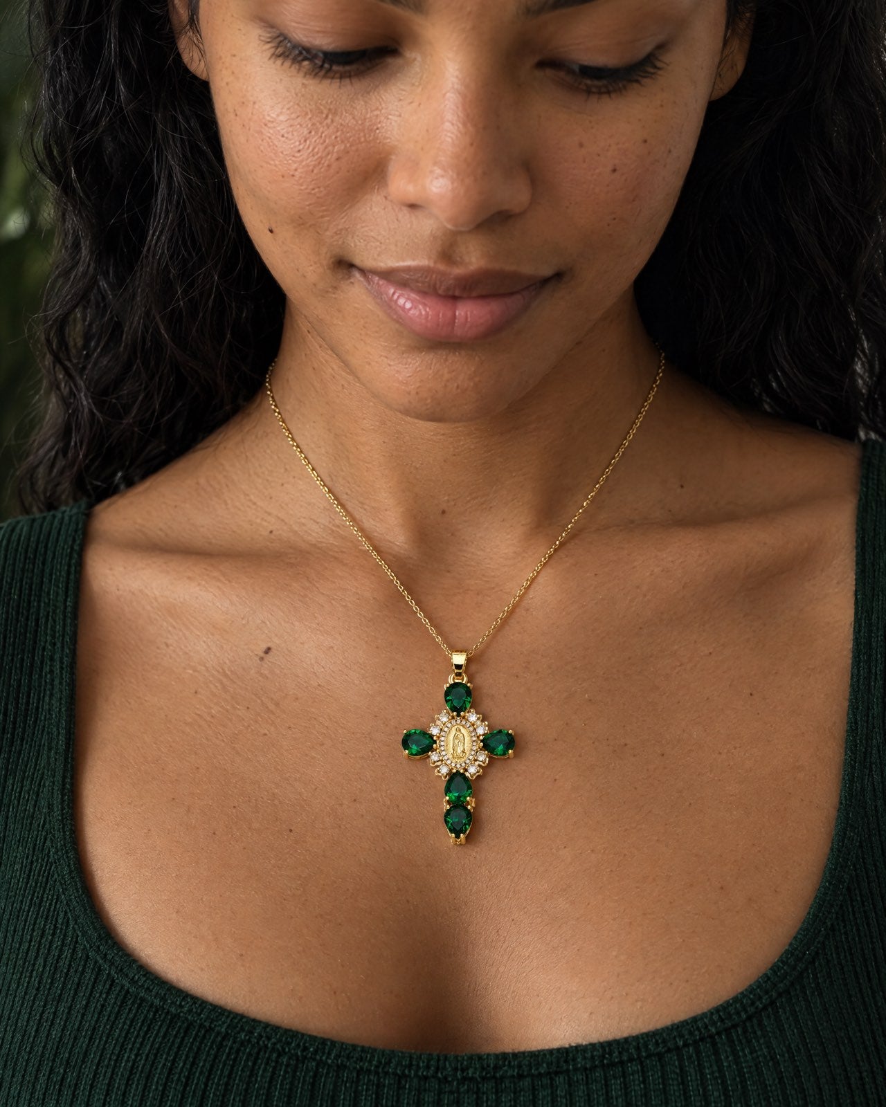 Pendentif croix doré avec pierres précieuses vertes, porté par Aline